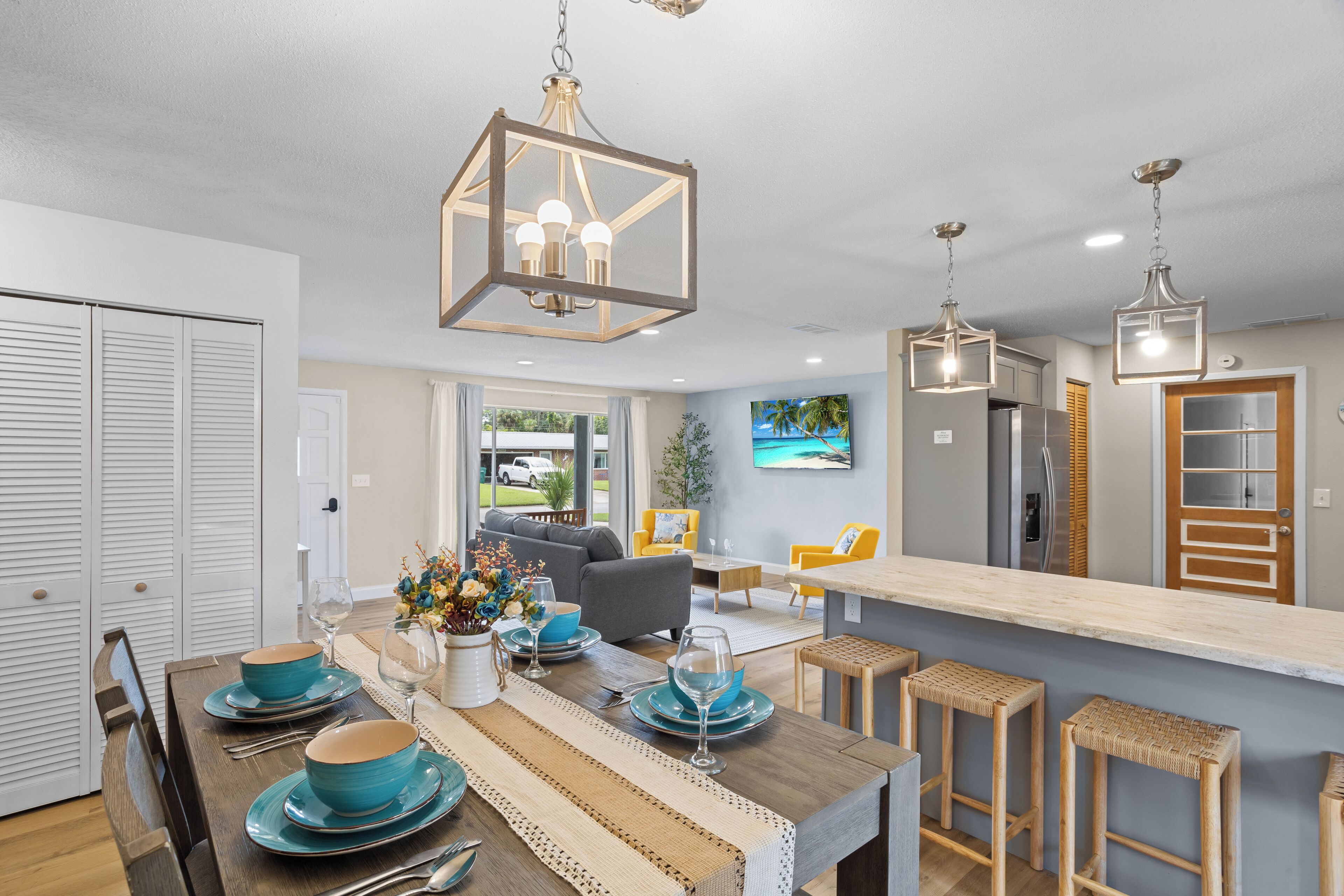 A modern kitchen with a central island, pendant lighting, and a dining area with blue tableware.