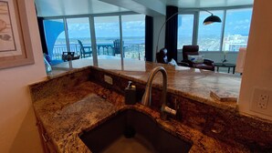 A modern kitchen with a granite countertop, stainless steel sink, and a view of the city through large windows. -  27th Floor 2BR 2BA incredible views! (Daytona Beach)