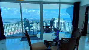 A dining area with a glass table and chairs, a vase with flowers, and a view of the ocean and cityscape through large windows. -  27th Floor 2BR 2BA incredible views! (Daytona Beach)