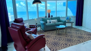 A spacious living room with a large window offering a view of the ocean, a red leather chair, a teal sofa, and a patterned rug. -  27th Floor 2BR 2BA incredible views! (Daytona Beach)