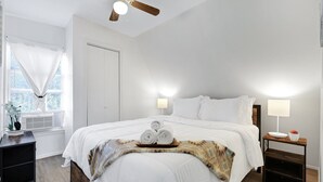 Un letto rifatto con cura, asciugamani arrotolati, un comodino con una lampada e una ventola a soffitto.