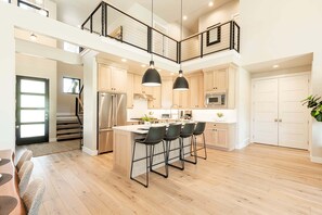 A modern kitchen with a central island, pendant lighting, and a staircase leading to an upper level.