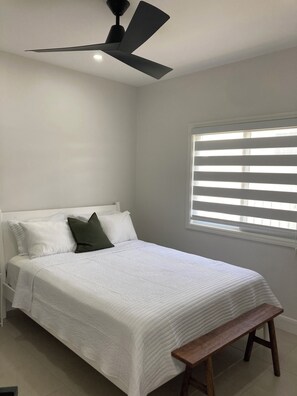 A bedroom with a bed, a bench, a ceiling fan, and a window with blinds. - Modern, Cozy, Airy 3-Bedroom Tropical Escape in Oceanpointe, Hanover, Jamaica (Lucea)