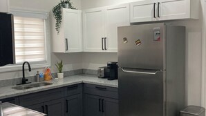 A modern kitchen with white cabinets, a stainless steel refrigerator, a built-in oven, a coffee maker, and a ceiling fan. - Modern, Cozy, Airy 3-Bedroom Tropical Escape in Oceanpointe, Hanover, Jamaica (Lucea)