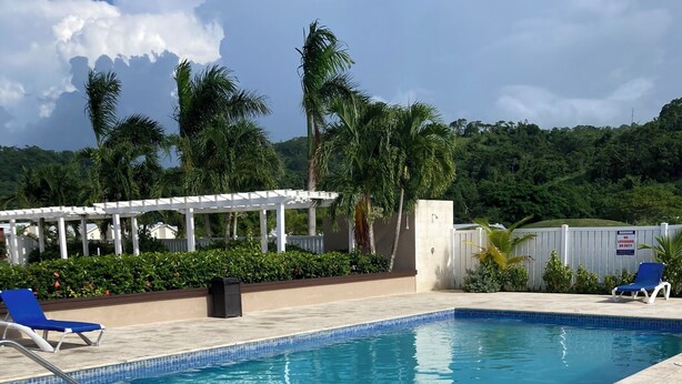 A swimming pool with tiled edges, surrounded by lounge chairs and a pergola. - Modern, Cozy, Airy 3-Bedroom Tropical Escape in Oceanpointe, Hanover, Jamaica (Lucea)