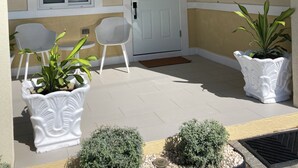 A covered outdoor area with a white door, a window, two chairs, and potted plants. - Modern, Cozy, Airy 3-Bedroom Tropical Escape in Oceanpointe, Hanover, Jamaica (Lucea)