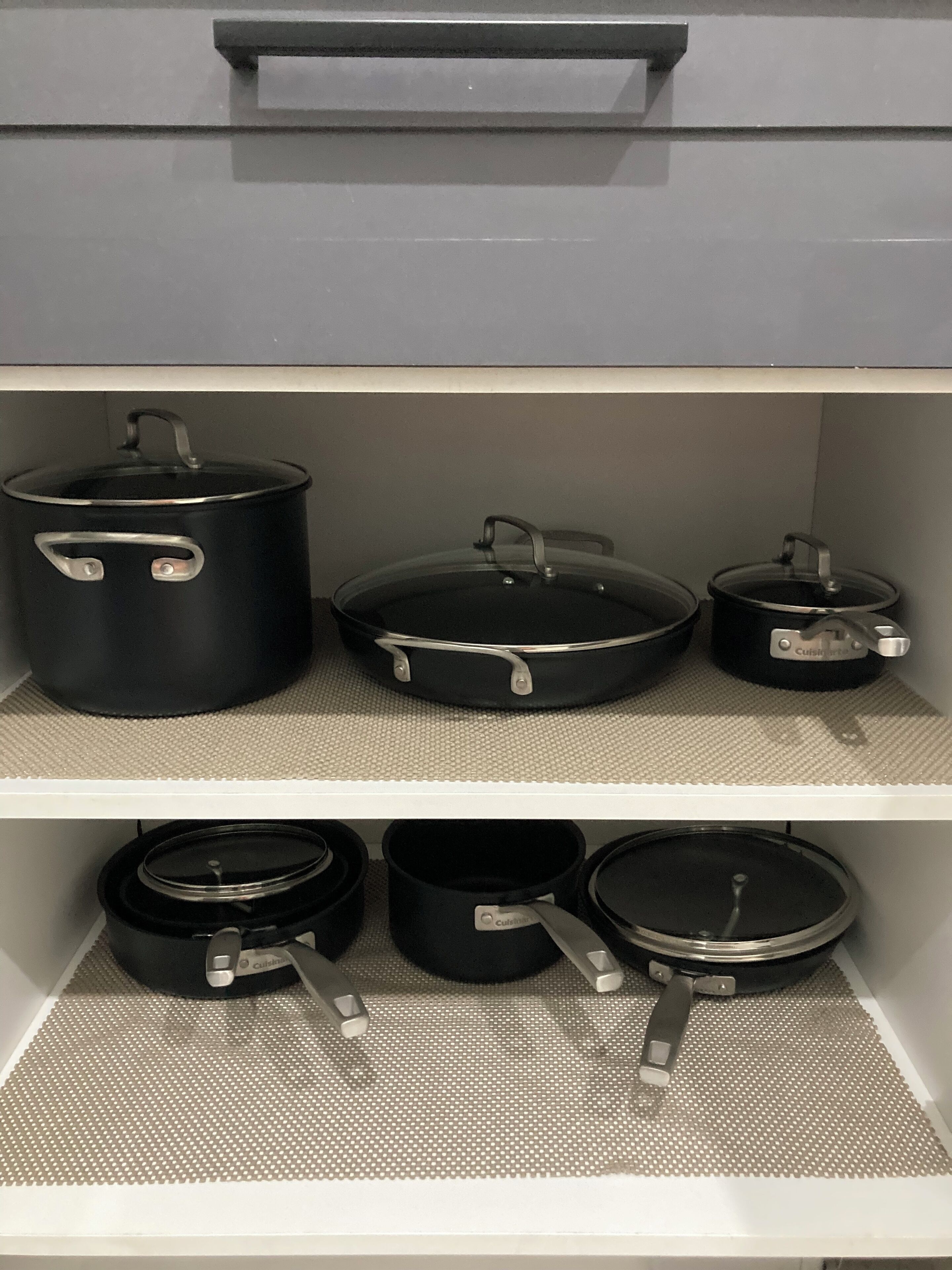 Un meuble de cuisine contenant plusieurs casseroles et poêles noires.