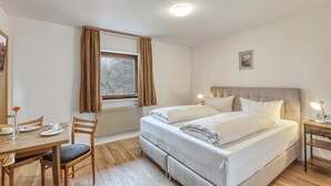 A bedroom with a bed, a desk, a chair, a radiator, and a window with curtains. - Beautiful apartment in Bischofsheim (Bischofsheim)