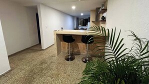 A narrow hallway leading to a kitchen area with a bar counter and two stools. - Casa Ik. A 5 min del aeropuerto, 8 min del Centro
 (Mérida)