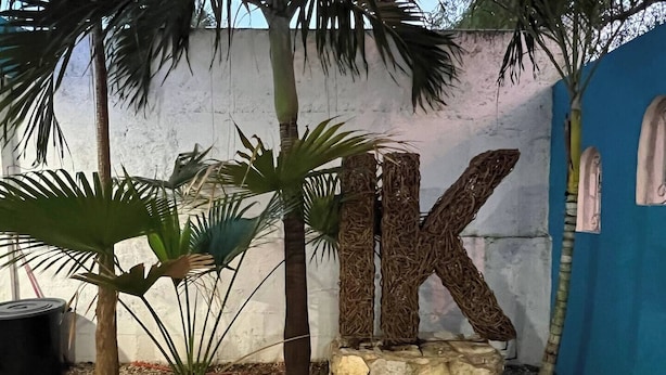 A decorative garden area with a stone base, a large 'K' structure, and palm plants. - Casa Ik. A 5 min del aeropuerto, 8 min del Centro
 (Mérida)