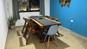 A dining area with a wooden table and chairs, a potted plant, and a blue wall with a decorative hanging. - Casa Ik. A 5 min del aeropuerto, 8 min del Centro
 (Mérida)
