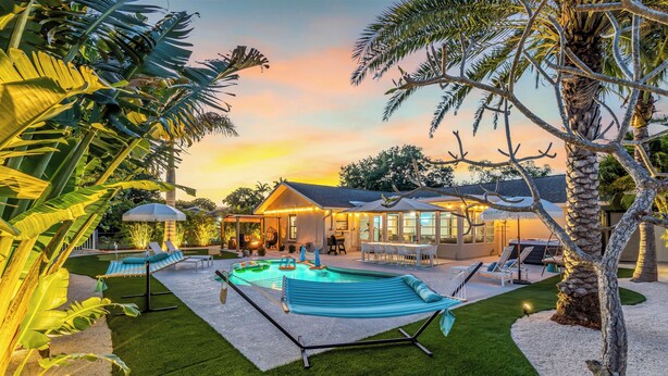 A pool area with a hammock, lounge chairs, and a house in the background. - Near AMI-Heated Pool-Hot Tub-Game Room-Putting Green-Outdoor Games (Bradenton)