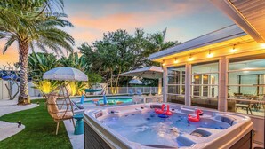 A hot tub with two flamingos, surrounded by a wooden deck, a pool, and outdoor furniture. - Near AMI-Heated Pool-Hot Tub-Game Room-Putting Green-Outdoor Games (Bradenton)