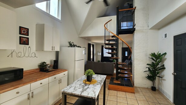 A modern kitchen with white cabinets, a marble countertop, and a spiral staircase leading to a loft area. - Timeless Tremont- Enjoy 20% off 5+ nights  (Cleveland)