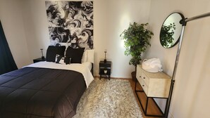 A bedroom with a large bed, a nightstand, a dresser, a mirror, and a wall with a marble-like pattern. - Timeless Tremont- Enjoy 20% off 5+ nights  (Cleveland)