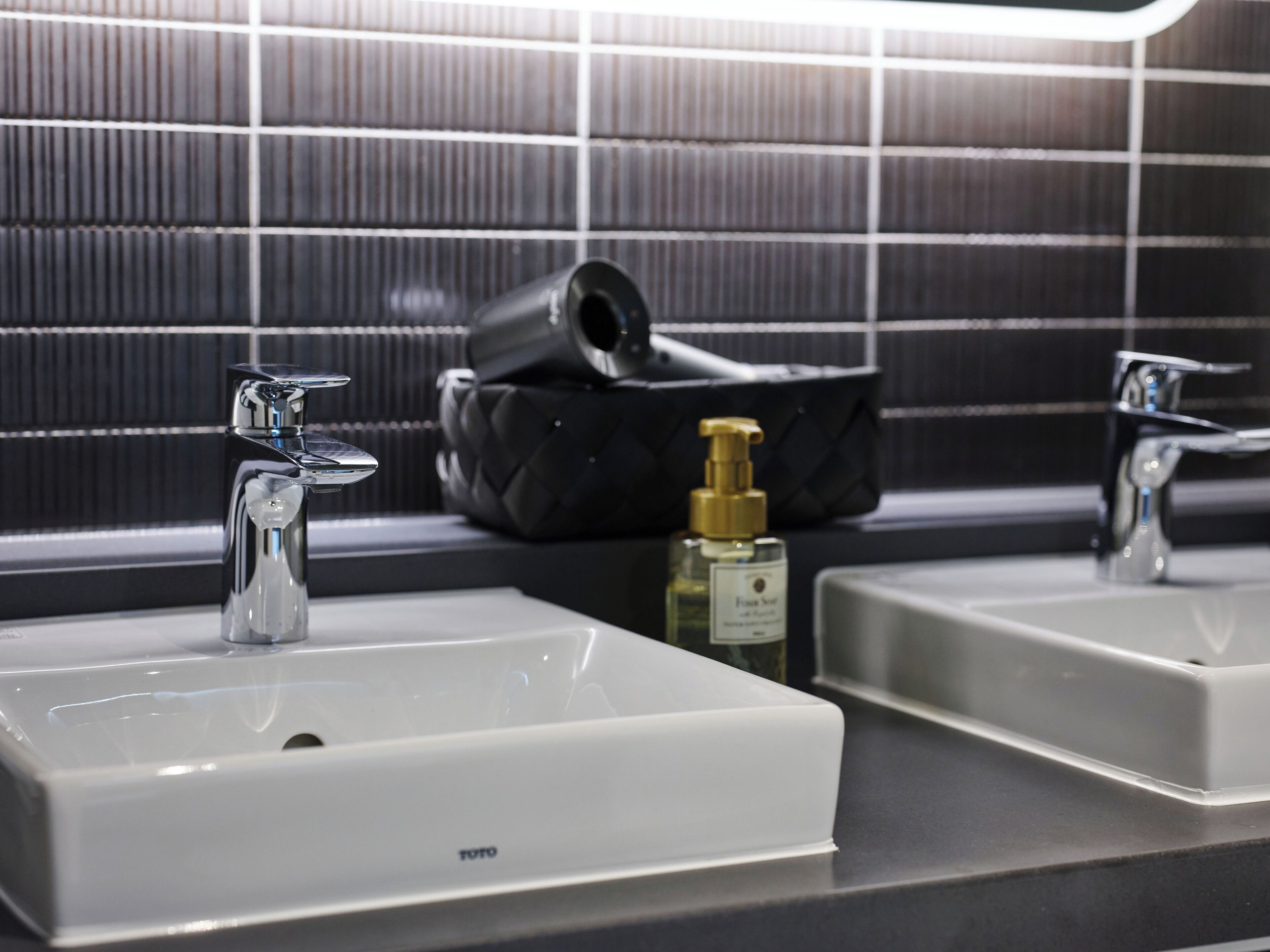 A bathroom with two sinks, a black handbag, and a bottle of hand soap.