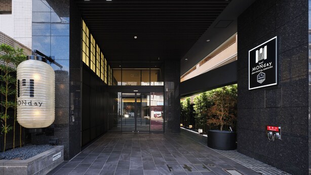 Una entrada de hotel moderna con un letrero destacado que dice 'MONday', puerta de cristal y un camino que conduce al vestíbulo.