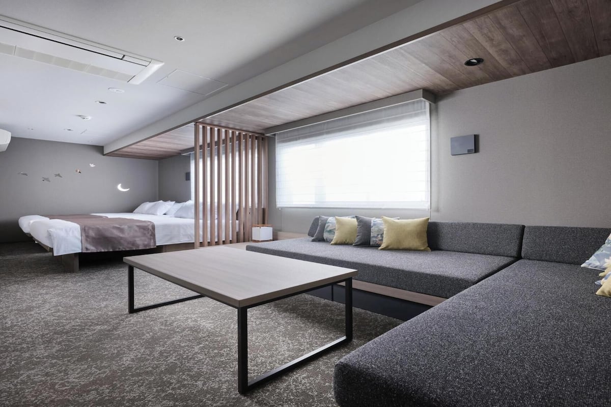 A modern hotel room with a bed, a sofa, a table, and a large window.