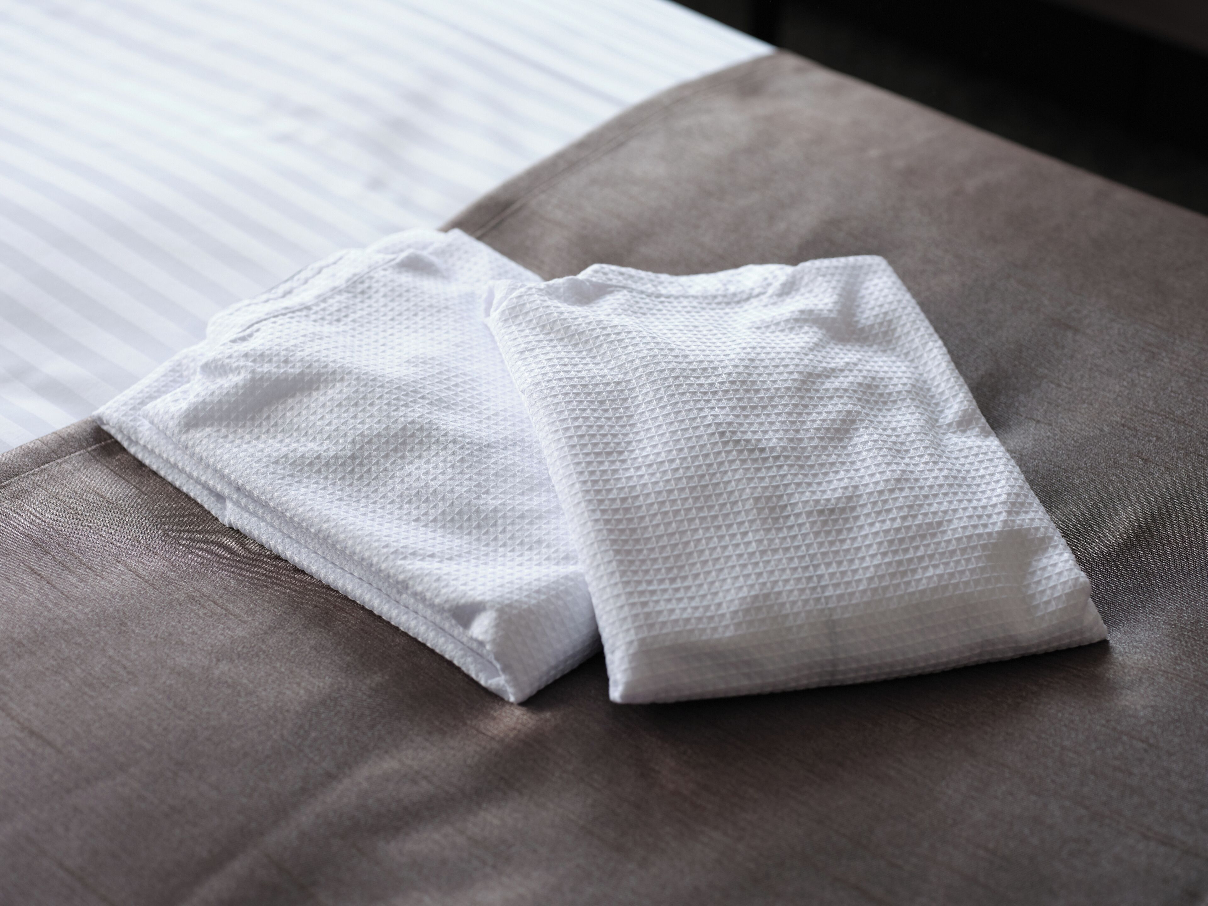 Toalha branca e bem dobrada sobre uma cama cinzenta com lençol listrado.