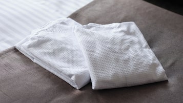 A neatly folded white towel on a gray bed with a striped sheet.