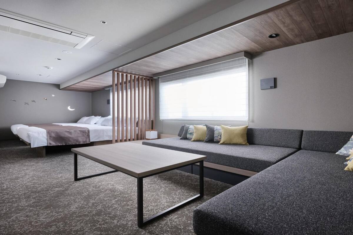 A modern hotel room with a bed, sofa, and a small table.