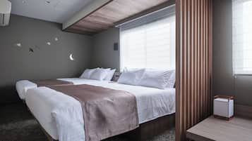 A hotel room with a bed, a bedside table, a window with blinds, a wall-mounted air purifier, and a ceiling light.
