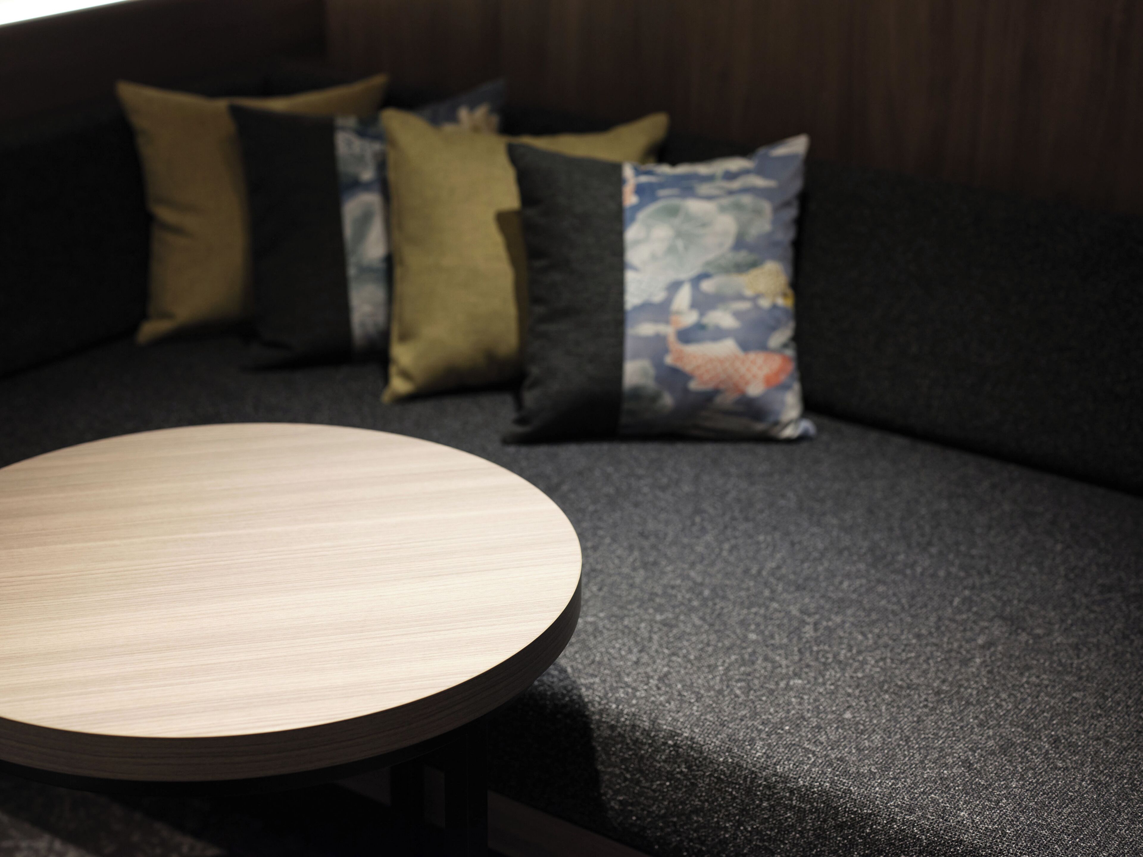 Una mesa redonda de madera en una habitación con un sofá gris oscuro y cojines estampados.