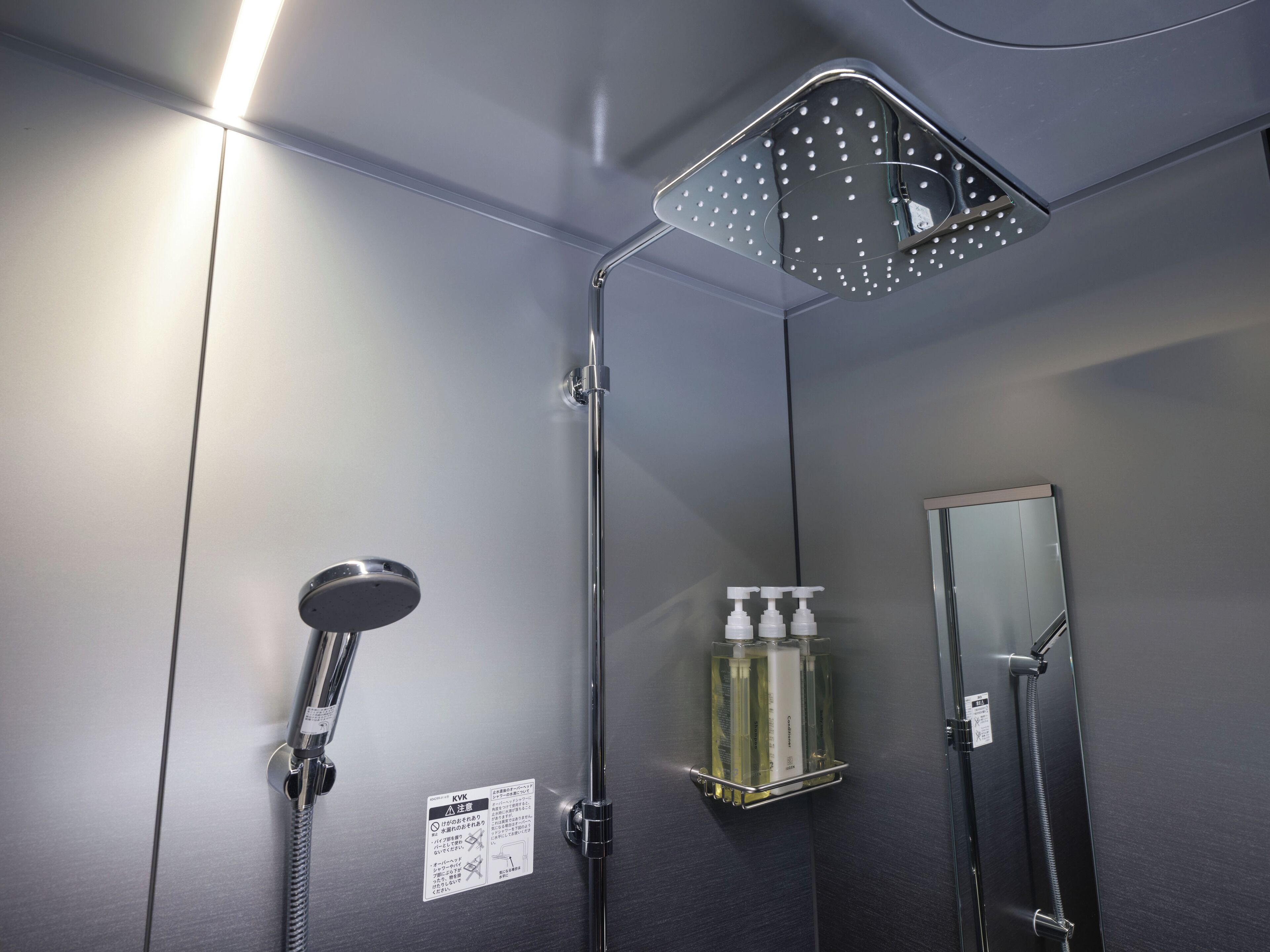 Une douche moderne équipée d’un pommeau de douche à main, d’un pommeau de douche à pluie et d’une étagère en verre pour les articles de toilette.