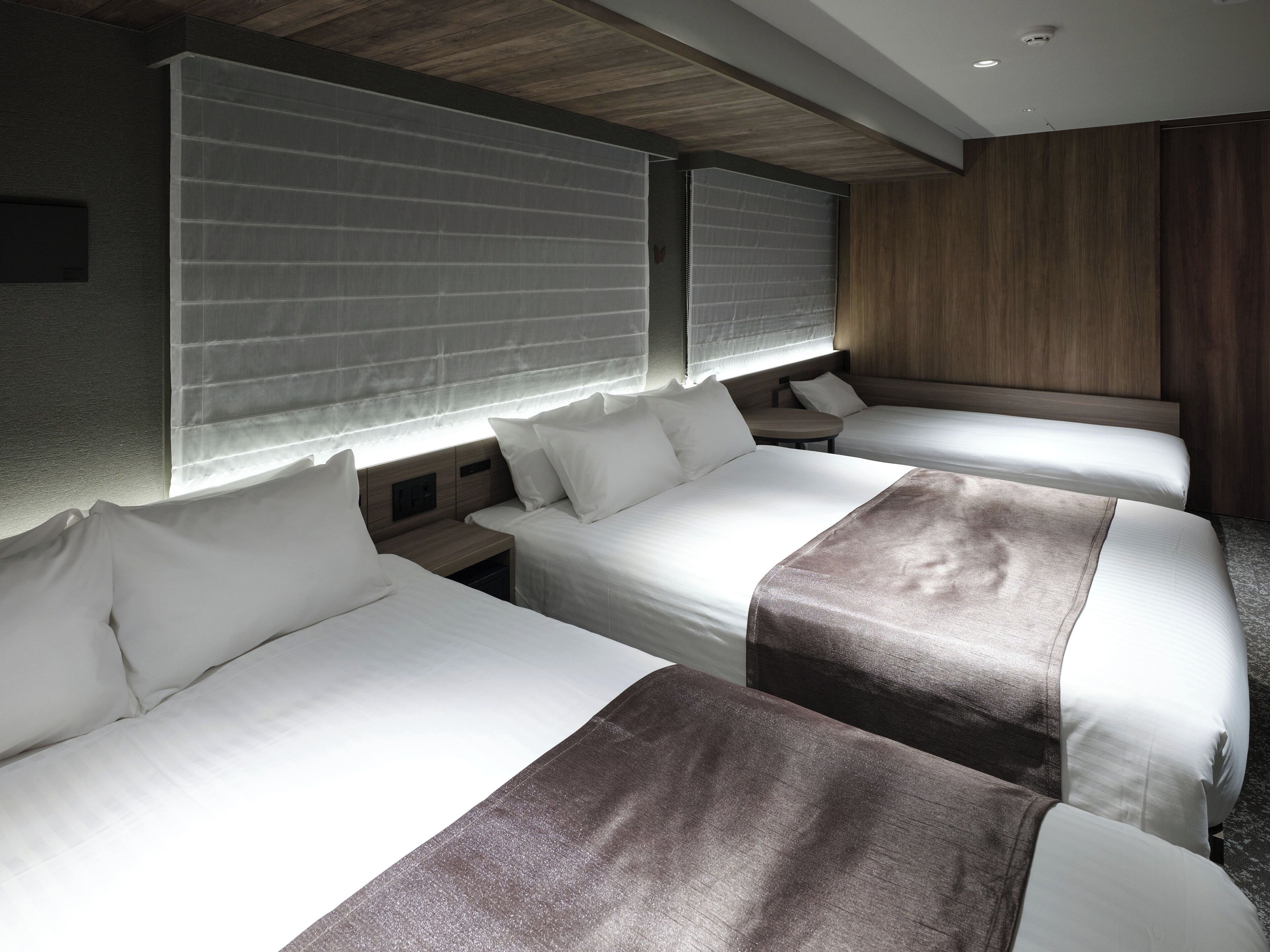 A hotel room with two beds, a small table, and a wooden headboard.