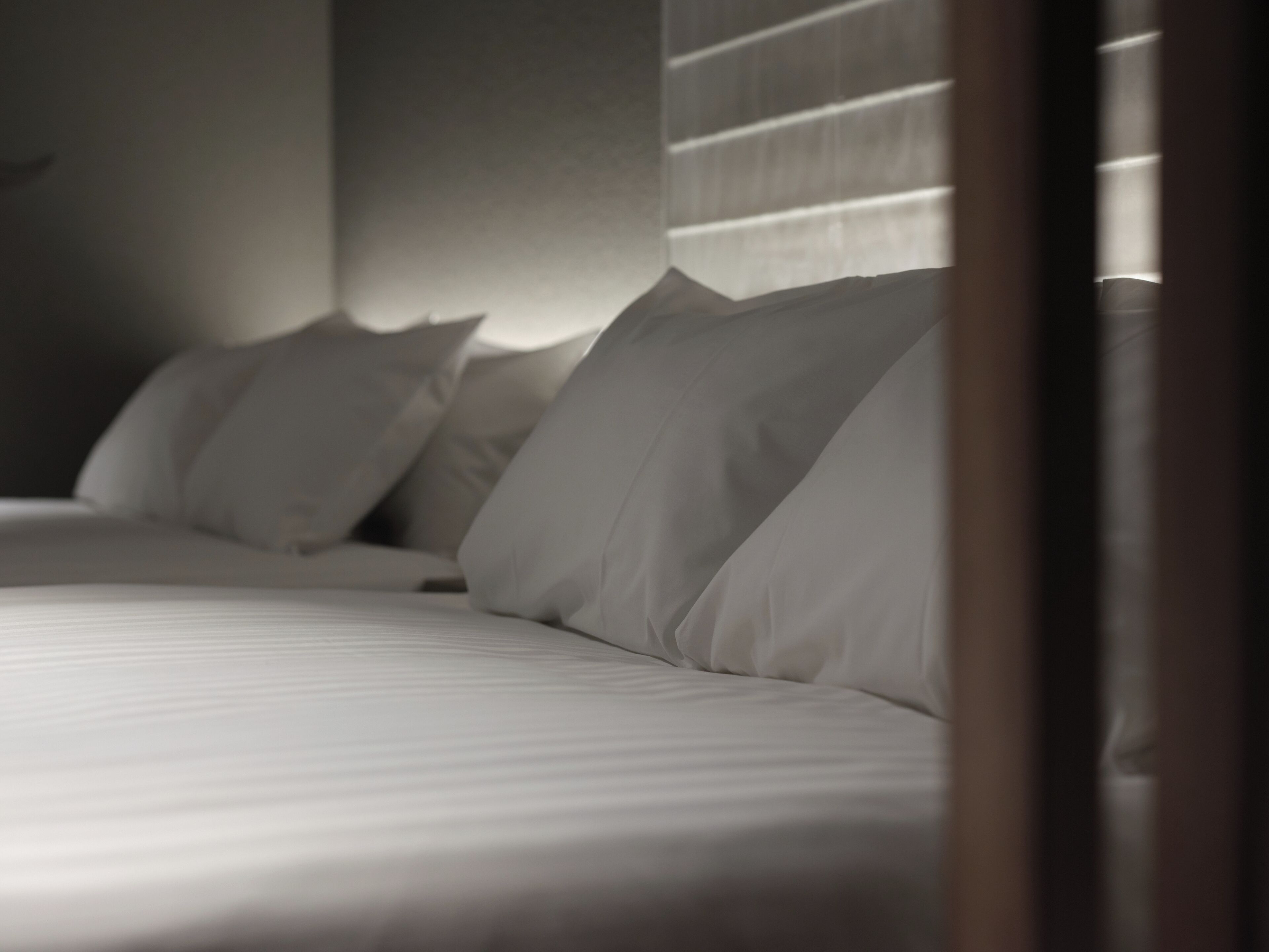 A bed with white linens and pillows, a headboard, and a window with blinds.
