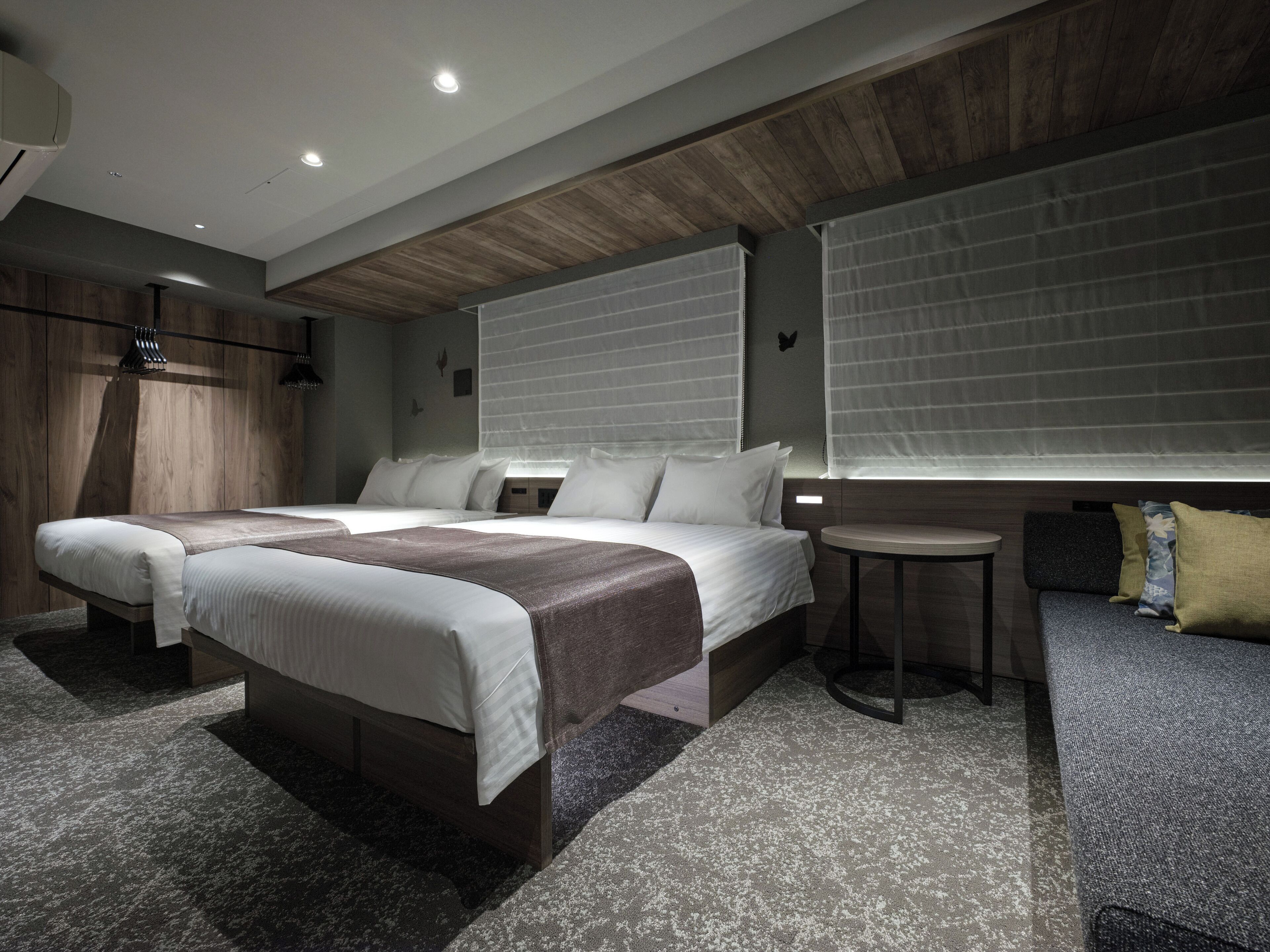 A modern hotel room with two beds, a small round table, and a sofa.