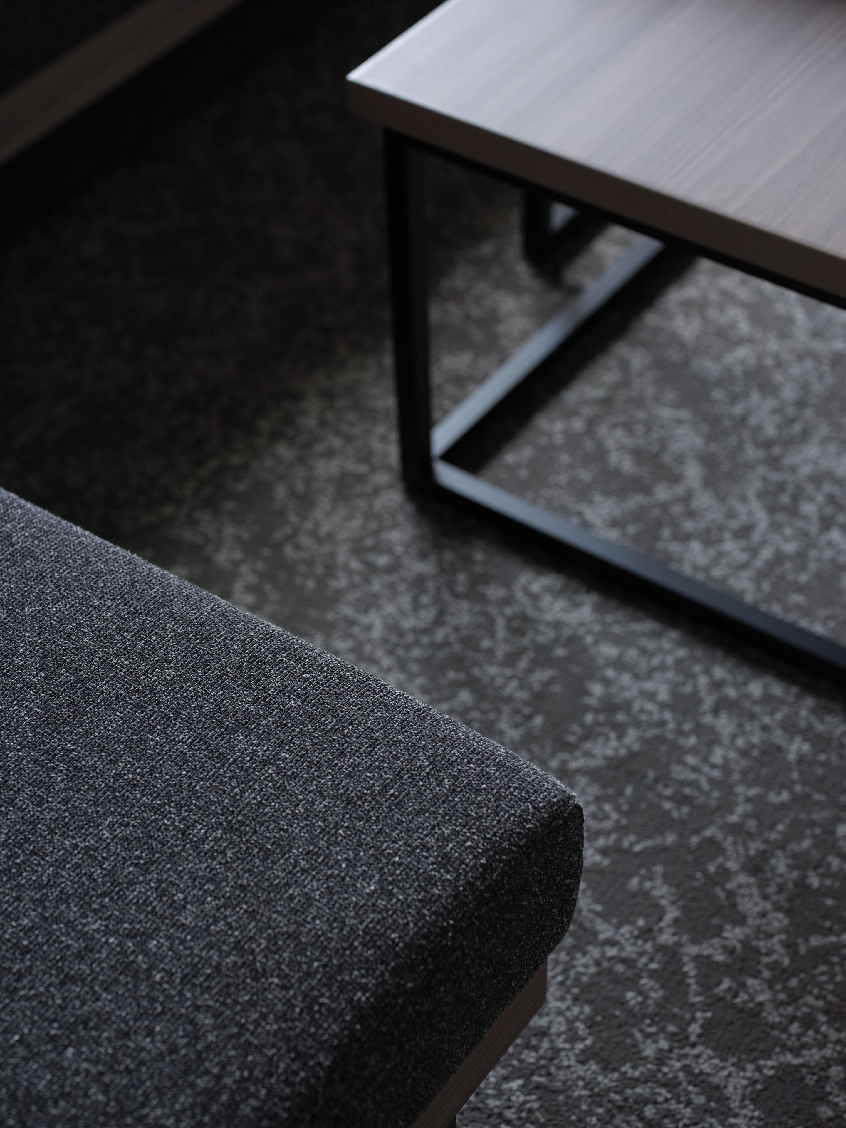 A close-up of a textured grey fabric, likely a sofa or chair, with a metal frame and a wooden table in the background.