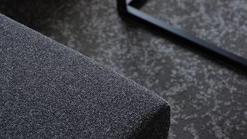 Gros plan sur un tissu gris texturé, probablement celui d’un canapé ou d’une chaise, avec une structure en métal et une table en bois en arrière-plan.
