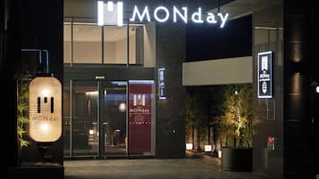 Entrada de hotel con un letrero llamativo que dice 'MONday', puertas de vidrio y un cartel rojo.