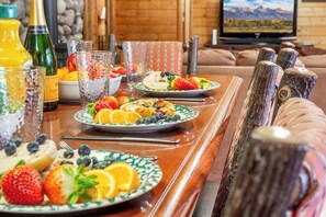 A breakfast table with plates of fruit and a bottle of orange juice.