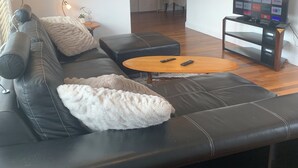Una sala de estar moderna con un sofá de cuero negro, una mesa de centro de madera y un televisor sobre un mueble.