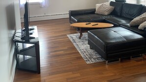 Una sala de estar moderna con un sofá de cuero negro, una mesa de centro de madera y un televisor de pantalla plana sobre un mueble.