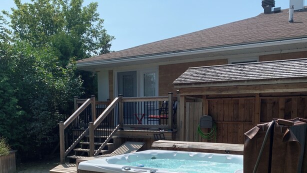 Un jacuzzi en un patio trasero con terraza de madera, una escalera y un área de patio techada.