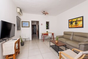 Un salon moderne doté d’un téléviseur à écran plat, d’un ventilateur de plafond, d’un canapé, d’une table à manger avec des chaises et d’un tableau accroché au mur.
