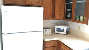 A kitchen with wooden cabinets, a white refrigerator, a toaster, a microwave, and a shelf with canned goods. - 1,800sf 3 Stories with 8 beds townhome (Casper)