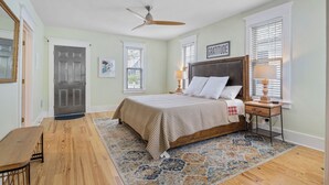 A bedroom with a bed, a nightstand, a lamp, a ceiling fan, and a door.