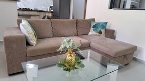 Een moderne woonkamer met een hoekbank, een glazen salontafel en een decoratieve vaas.
