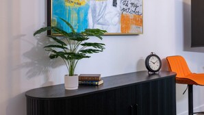 Ein modernes Wohnzimmer mit einem schwarzen Konsolentisch, einem Topfpflanzen, einer Uhr und einem orangefarbenen Sessel.
