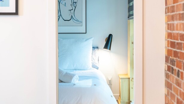 Ein Schlafzimmer mit einem Bett, einem Nachttisch, einer Lampe und einem gerahmten Bild an der Wand.