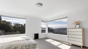 A bedroom with a bed, a radiator, a dresser, and large windows with a city view. - St Clair Heights-Ocean views (Dunedin)