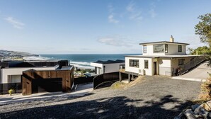 A modern coastal property with a view of the ocean, featuring a multi-level house with a flat roof and a prominent staircase leading to the entrance. - St Clair Heights-Ocean views (Dunedin)