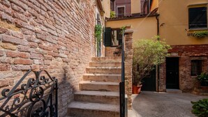 Une ruelle étroite, avec un mur de briques d’un côté et l’entrée d’un immeuble de l’autre. Un escalier en pierre mène à l’entrée, et une rambarde métallique est visible sur la gauche.