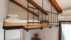 Un lit superposé avec une tête de lit en bois et des barreaux en métal, une petite table avec un vase et une fenêtre avec des rideaux.