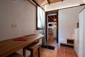 A narrow hallway with a wooden table and bench, a door leading to another room, and a tiled floor.