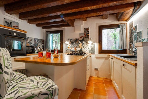A kitchen with a wooden island, a built-in oven, and a window with curtains. - Ca' del Majo (Venezia)